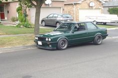 a green car is parked on the side of the road in front of a house