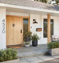 two planters on the front porch of a white brick house with wooden doors and windows