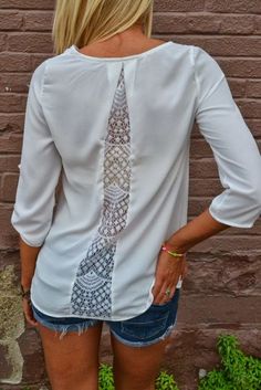 a woman standing in front of a brick wall wearing a white shirt with an intricate tie on it