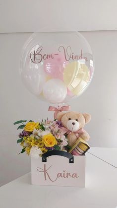 a teddy bear sitting on top of a box with flowers and balloons in the air