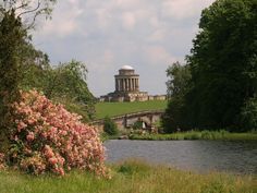 a large building sitting on top of a lush green hillside next to a river and bridge