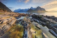 the sun is shining on some rocks by the water and mountain range in the background