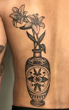 a man's back with tattoos and flowers in a vase