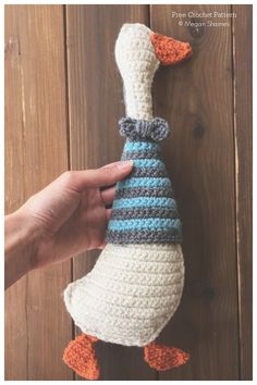 a hand holding a crocheted duck with a hat on it's head