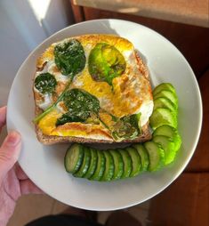 a person holding a white plate with a sandwich and cucumber on it,