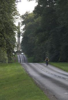 a bicyclist rides down the road in front of a monument on a hill