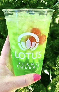 a hand holding up a green drink in front of a tree with the words lotus on it