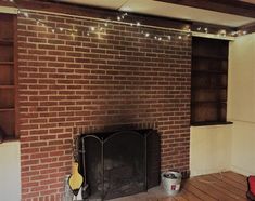 an empty living room with a fire place and bookshelf in the corner, surrounded by string lights