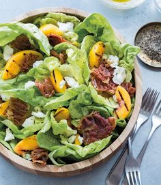 a wooden bowl filled with lettuce and peaches on top of a table