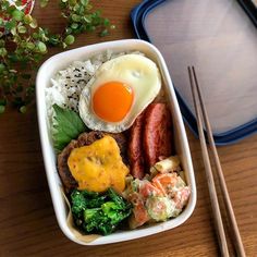 a bento box filled with rice, meat and vegetables next to chopsticks