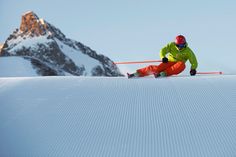 a man riding skis down the side of a snow covered slope with a mountain in the background