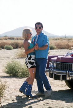 a man and woman standing in front of a red car with a cow print skirt