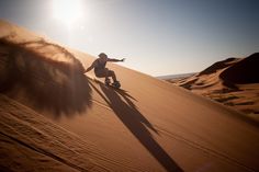 a man riding a skateboard down the side of a sand dune in the desert