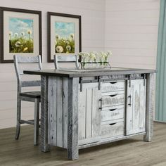 a kitchen island made out of wood with two pictures on the wall above it and chairs around it