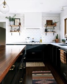 a kitchen with black cabinets and white subway backsplash, wood countertops, and open shelving