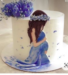 a white cake with blue flowers and a pregnant woman on the top is decorated in fondant