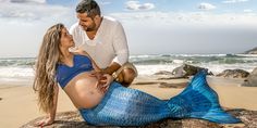 a pregnant woman laying on top of a rock next to a man