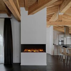 a modern fireplace in the middle of a living room with chairs and tables around it