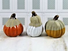 three ceramic pumpkins sitting side by side on a counter top in front of a wall