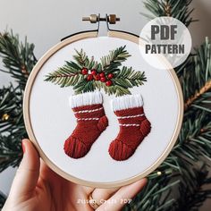 a hand embroidered christmas stocking ornament hanging from a hoop with pine needles