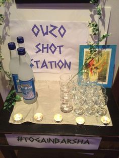 a table with candles and bottles on it next to a sign that says ouzo shot station