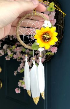 a hand holding a white dream catcher with a yellow sunflower on it's side