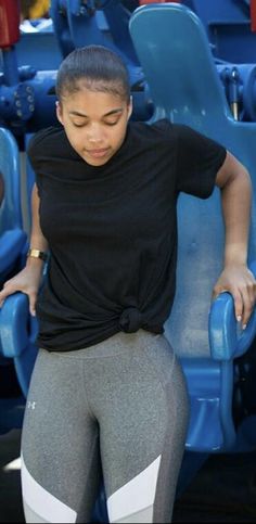 a woman is sitting in the stands at a baseball game wearing leggings and a black t - shirt