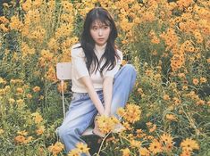 a young woman sitting on a bench in a field of wildflowers with yellow flowers