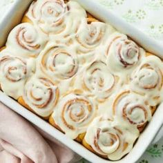 a pan filled with cinnamon rolls sitting on top of a white table next to a person's hand