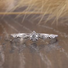 a white gold engagement ring with an old - fashioned style diamond center and leaves on the band