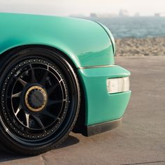 the front wheel of a green sports car parked in a parking lot next to the ocean