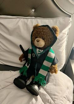 a brown teddy bear wearing a green and white scarf sitting on top of a bed