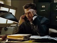 a man sitting at a desk talking on the phone and holding his hand to his head