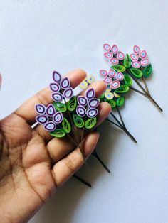 the hand is holding three small colorful flowers