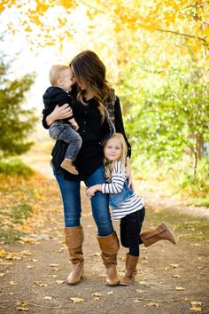 a mother and her two children walking down a path in the woods with fall leaves