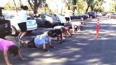 several people doing push ups in the middle of a parking lot with cars behind them