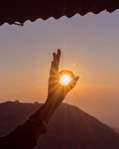 the sun is setting behind a person's hand with their fingers in the air