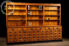 an old wooden bookcase with many drawers and bottles on the bottom shelf, in front of a black background