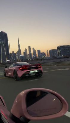 a pink sports car driving down the road in front of a large cityscape