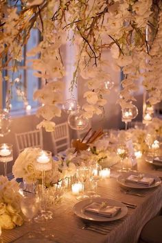 a long table with white flowers and candles on it is set for an elegant dinner