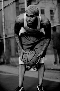 a man holding a basketball while standing on a street next to a chain link fence