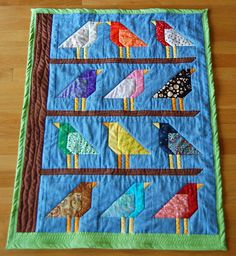 a quilted table runner with colorful birds on the top and bottom, sitting on a wooden floor