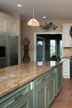 a kitchen with green cabinets and marble counter tops, an island in the middle has a clock on it