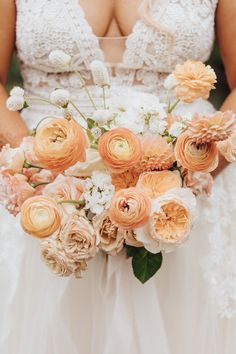 a bride holding a bouquet of peach and white flowers on her wedding day at the park