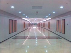 an empty long hallway with white walls and lights on the ceiling is lit by recessed lighting