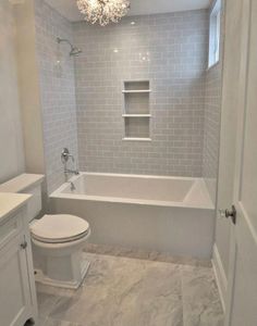 a white toilet sitting next to a bath tub in a bathroom under a chandelier