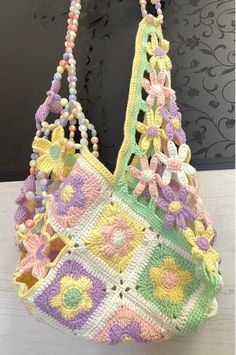 a multicolored crocheted bag hanging from a hook on a wall with beads