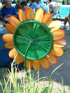 an orange and green flower sitting on top of a grass covered field next to people