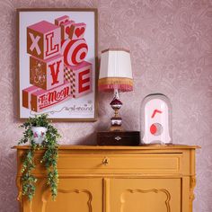 a yellow dresser topped with a lamp next to a painting