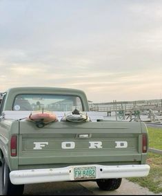 an old ford pickup truck parked on the side of the road in front of a dock